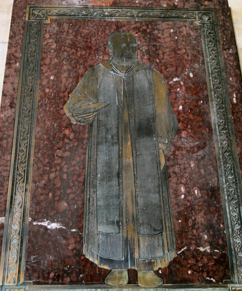 Placa de latão gravada com a figura do bispo James Hannington, de batina e sobrepeliz, sobre mármore vermelho