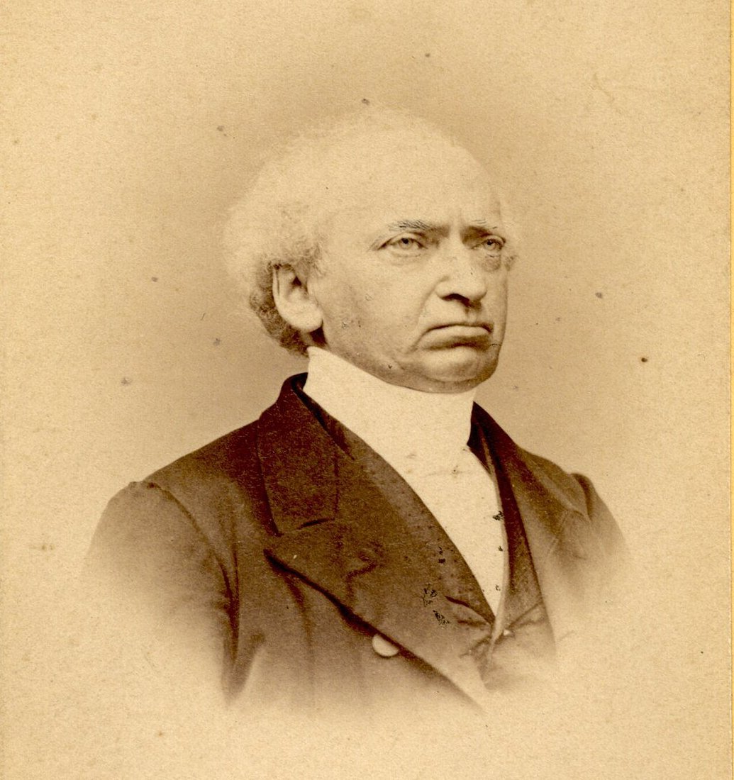 Retrato fotográfico em sépia do teólogo e hebraísta Franz Delitzsch, já idoso, de cabelos brancos e casaco escuro