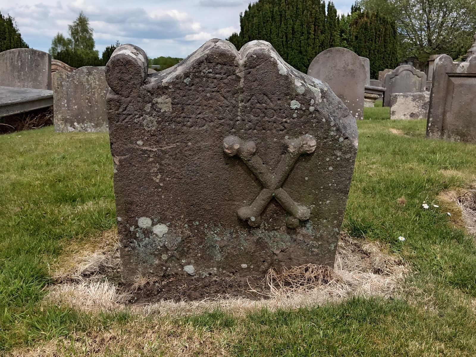 Lápide antiga com ossos cruzados esculpidos, no cemitério de St Kentigern, em Lanark, na Escócia
