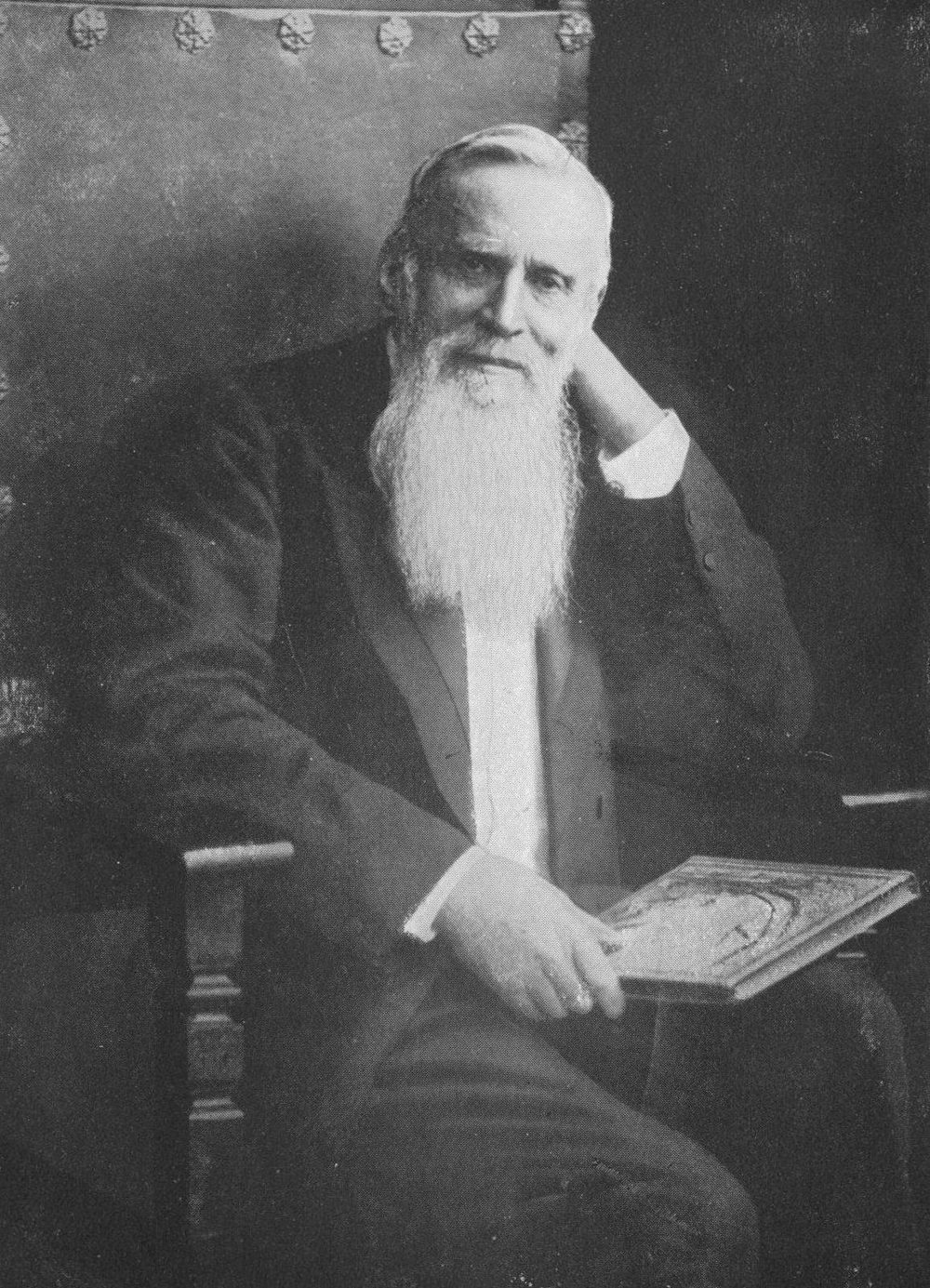 Retrato em preto e branco de Friedrich Wilhelm Baedeker já idoso, de barba branca longa, sentado com um livro no colo