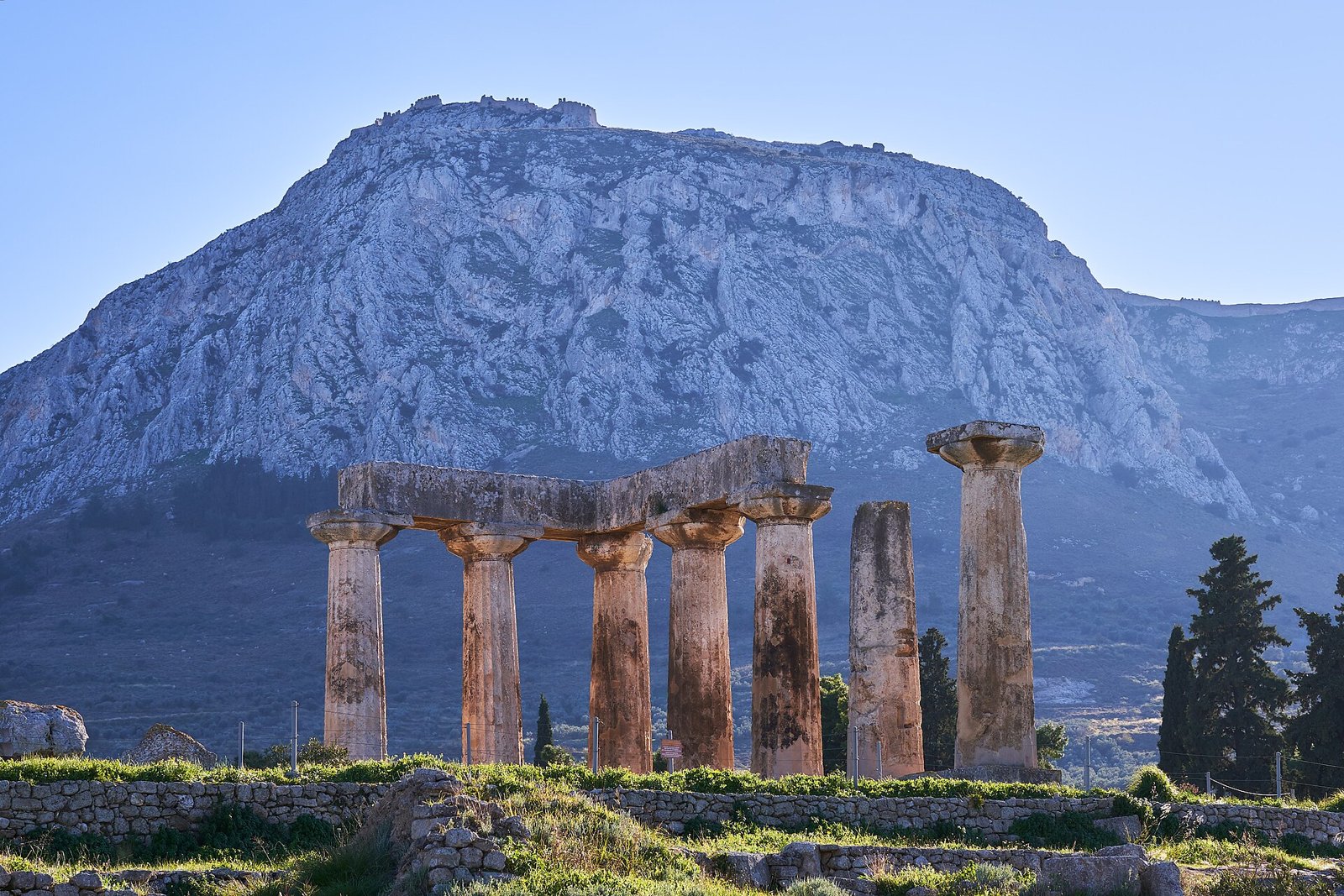 Ruínas do templo de Apolo na antiga Corinto, com a colina da Acrocorinto ao fundo