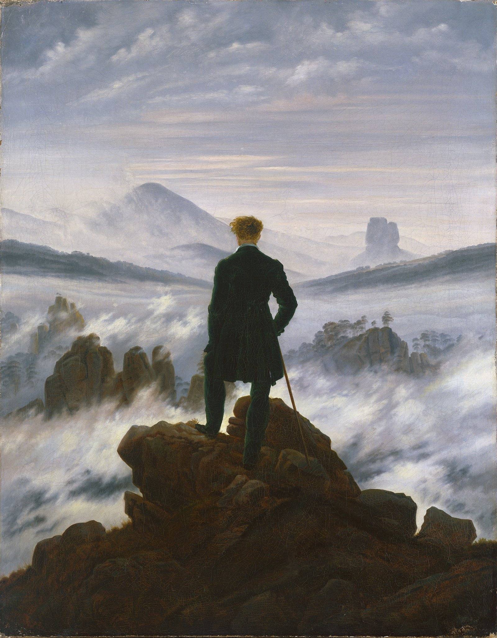 Um homem de casaco escuro, visto de costas, em pé sobre uma rocha, contempla montanhas e um mar de neblina