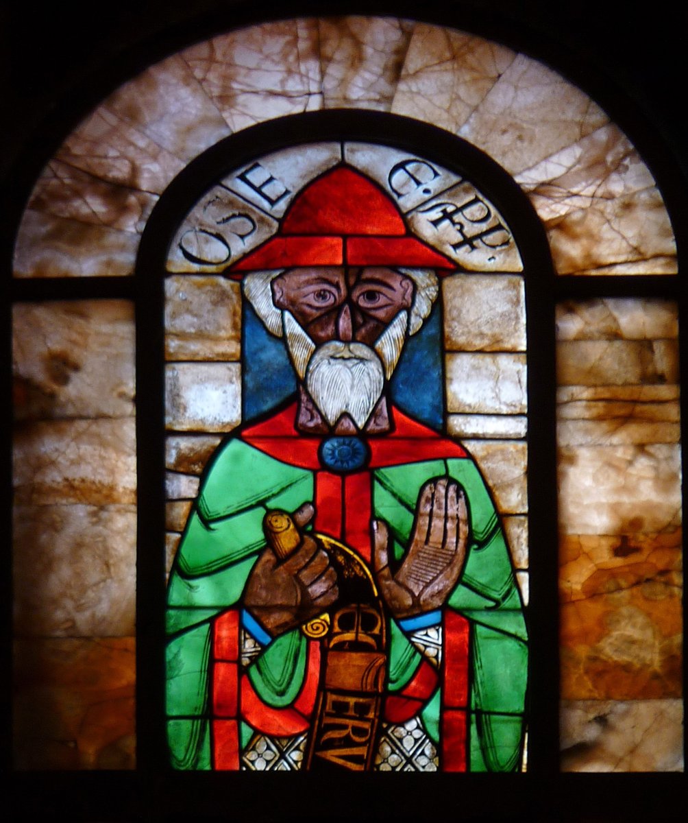 O profeta Oséias em vitral do início do século 12, com barba branca, chapéu vermelho e um pergaminho nas mãos