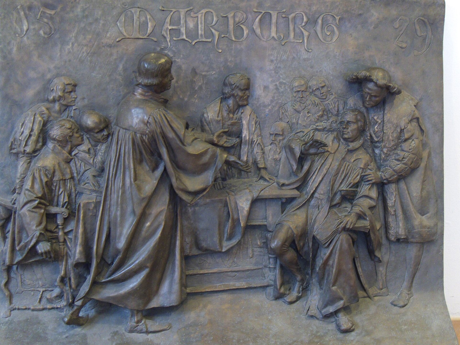 Relevo em bronze com Zuínglio de pé, diante da mesa, e Lutero sentado, sob a inscrição Marburg 1529