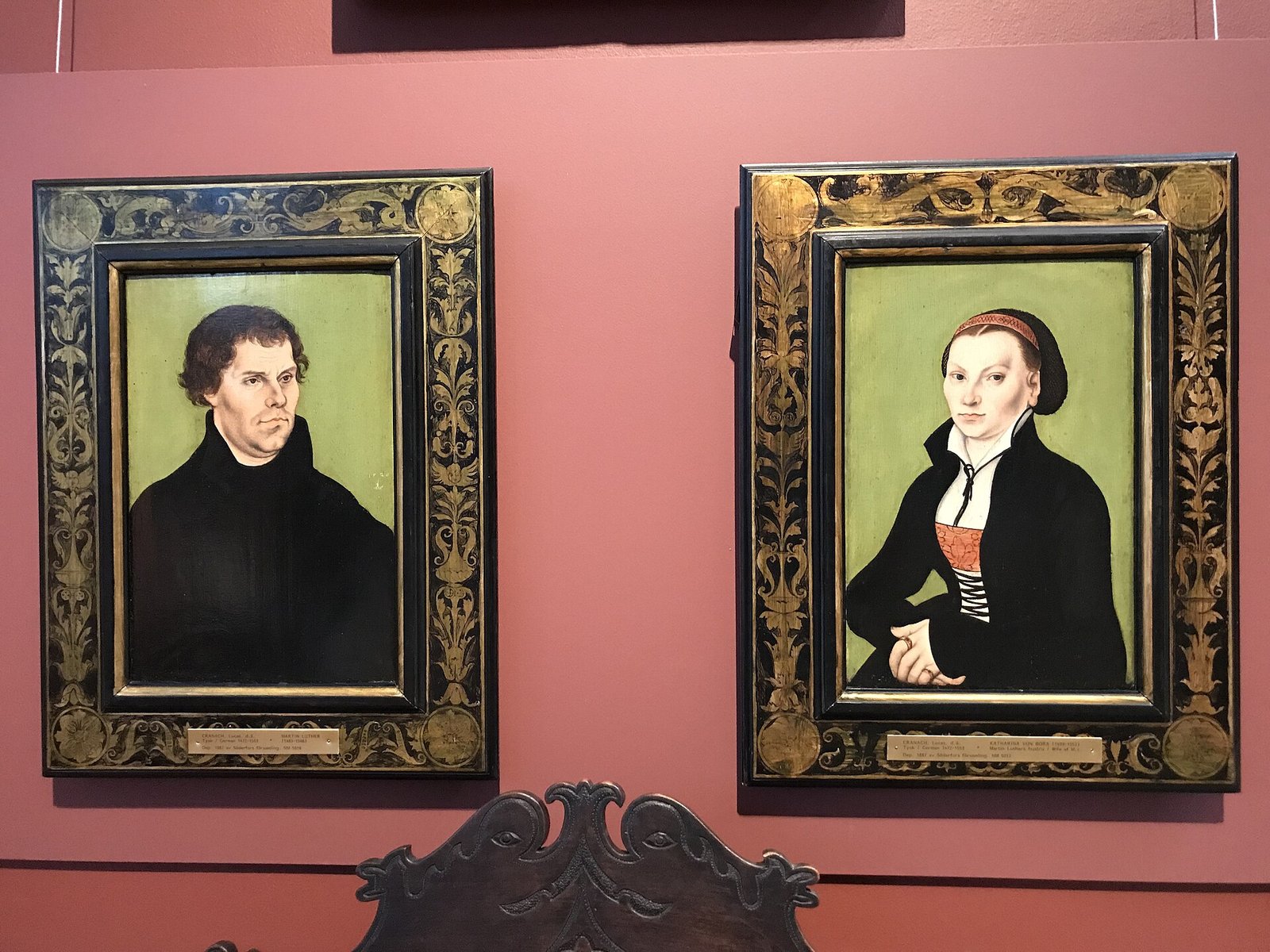 Dois retratos pintados lado a lado: Martinho Lutero, de roupa escura, e Catarina von Bora, de touca e colete vermelho, sobre fundo verde