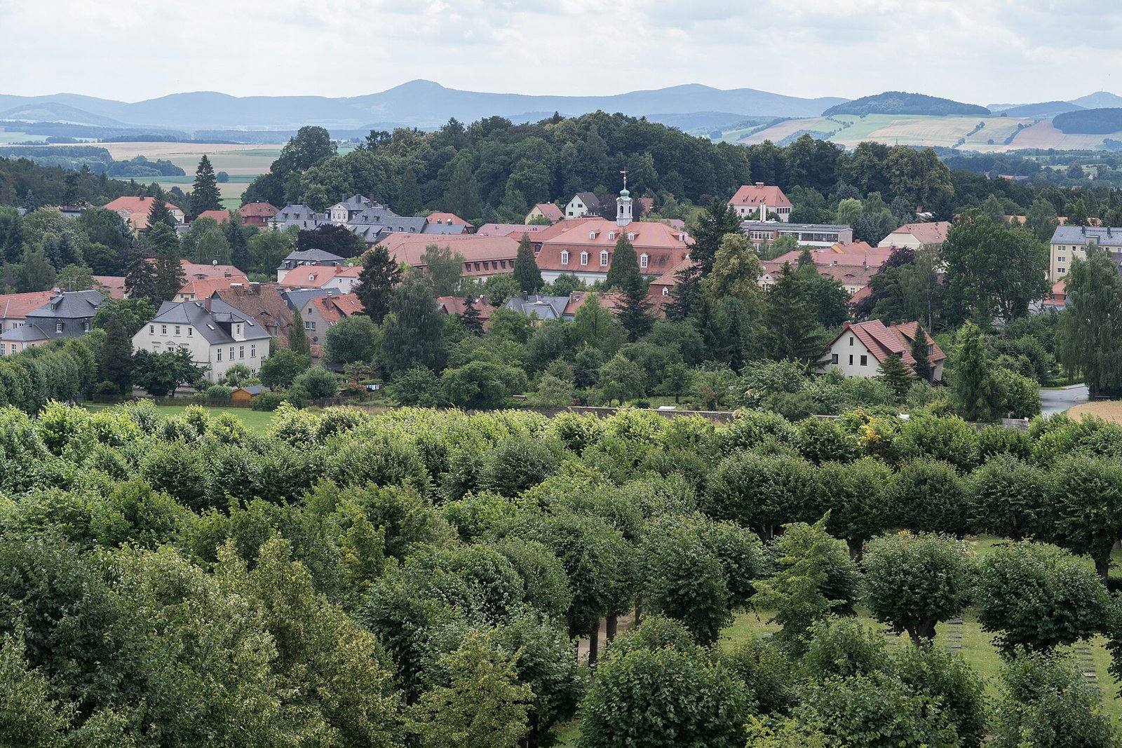 Vista da vila de Herrnhut, na Saxônia, com telhados vermelhos entre árvores e o cemitério morávio em primeiro plano